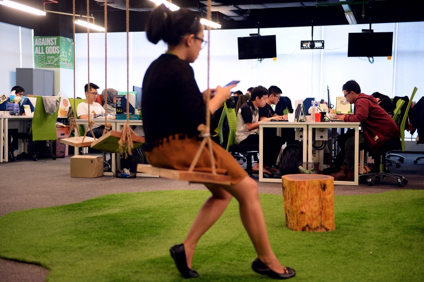 An employee uses a smartphone while sitting on a swing as others work at PT Tokopedia's offices in Jakarta, Indonesia, on Friday, Feb. 19, 2016. (Dimas Ardian/Bloomberg via Getty Images)