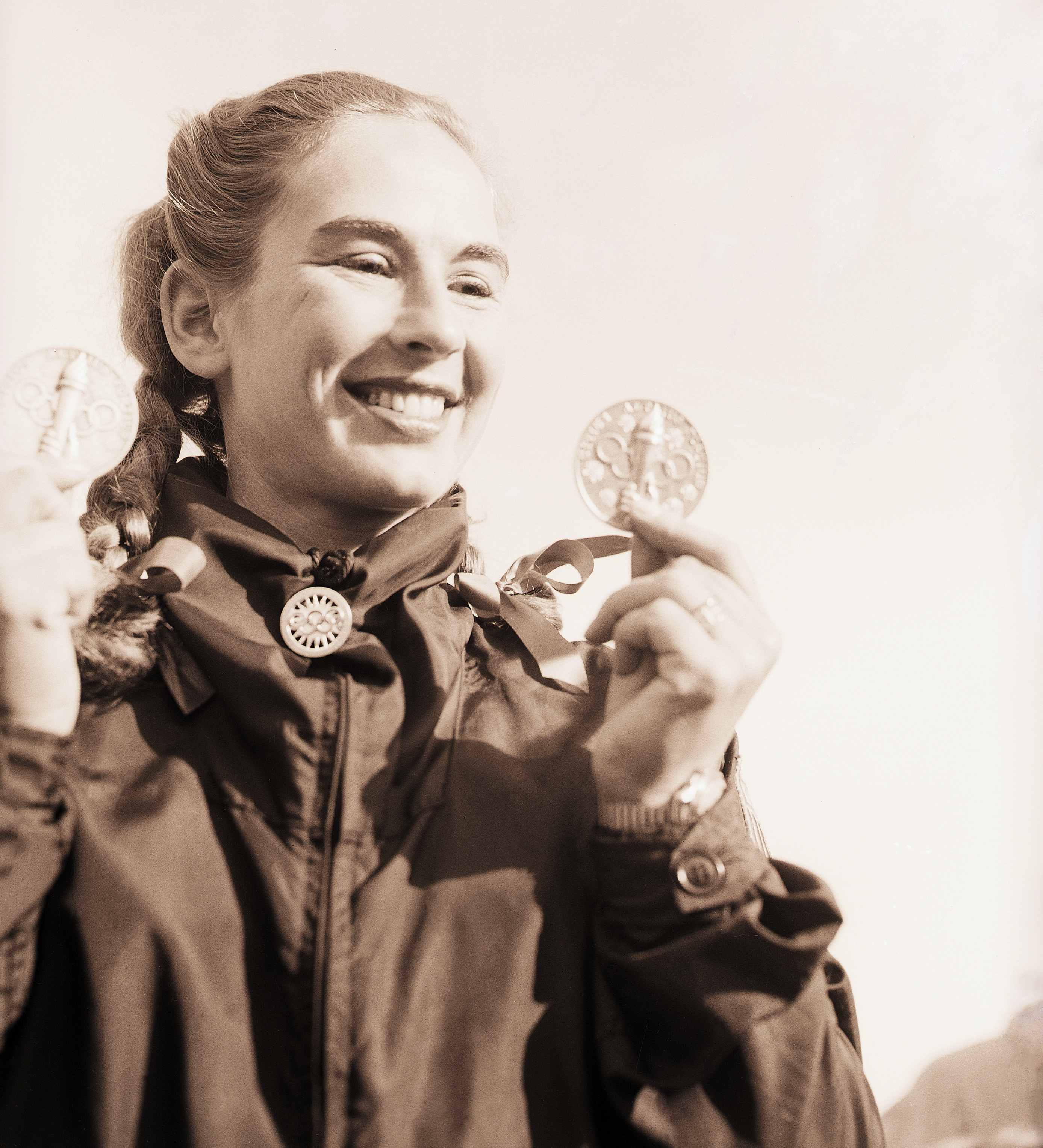 Gretchen Fraser displays the two medals she won in Olympic skiing events. One medal was for placing 2nd in the alpine combined downhill and the other was 1st prize in the special Woman's slalom. Fraser became the first American ever to win an individual skiing championship in the history of the Olympic games.