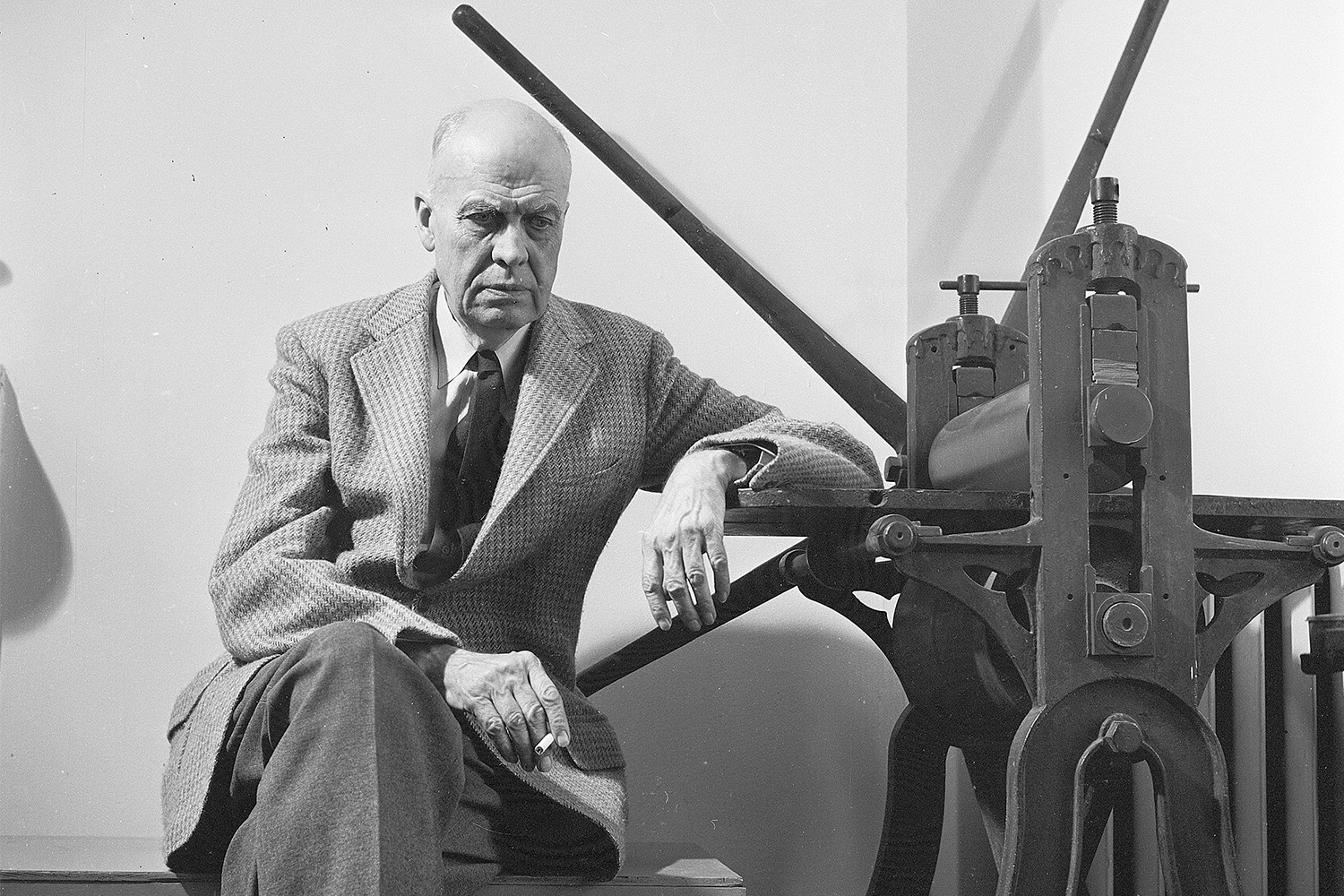 American realist painter Edward Hopper (1882-1967) sitting by a manual printing press in his Greenwich Village studio