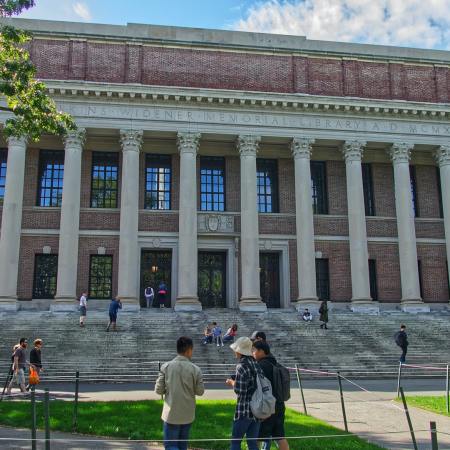 Students on the grass in front of and on the stairs of Widener Library at Harvard during the day