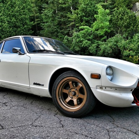 A white 1978 Datsun 280Z sports car sitting on asphalt in front of green trees. In this story, the Datsun owner talks about what it's like to own the '70s car.