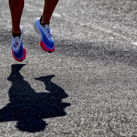 A view of two Nike running sneakers on black pavement, over a shadow of a runner.