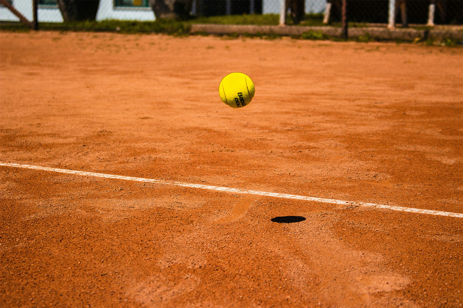 A closeup of a tennis ball bouncing off a clay surface.