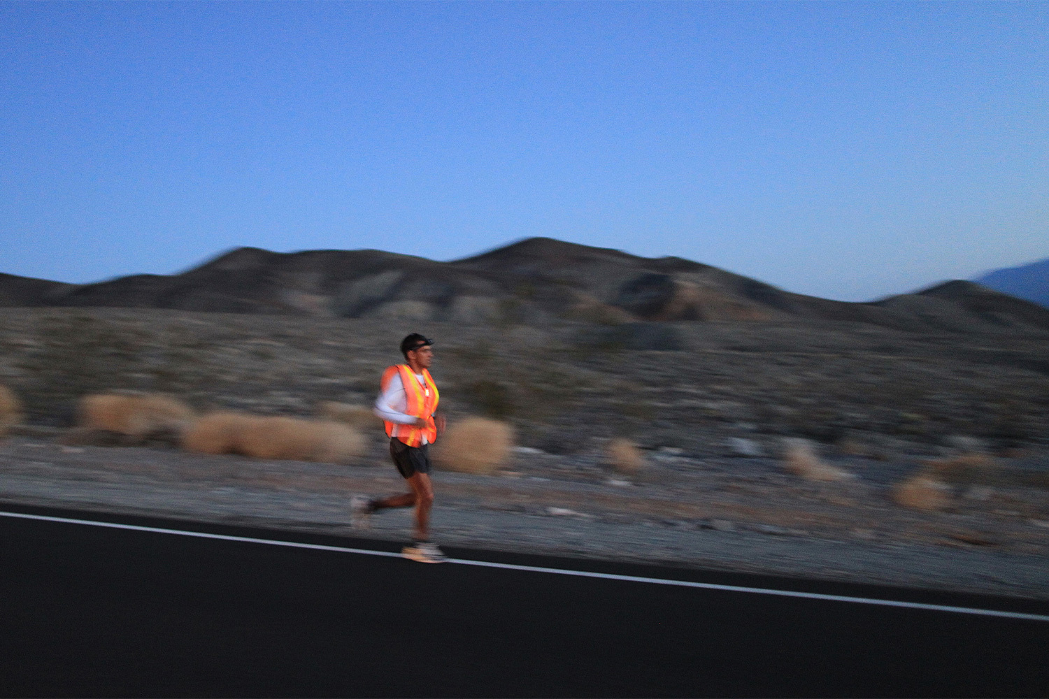 A man running through the desert at dusk in a neon orange singlet.