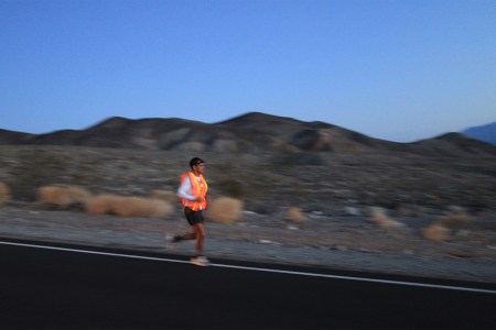 A man running through the desert at dusk in a neon orange singlet during an endurance race.