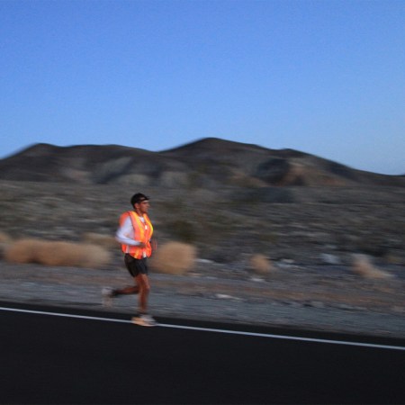 A man running through the desert at dusk in a neon orange singlet during an endurance race.