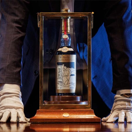 A man (neck down) standing over a bottle of The Macallan Adami 1926, which just broke a spirits auction record