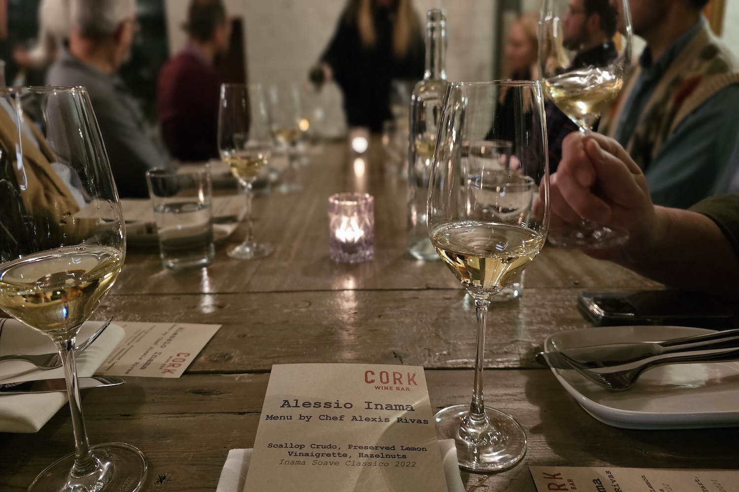 hands holding wine glasses with white wine, menus on table