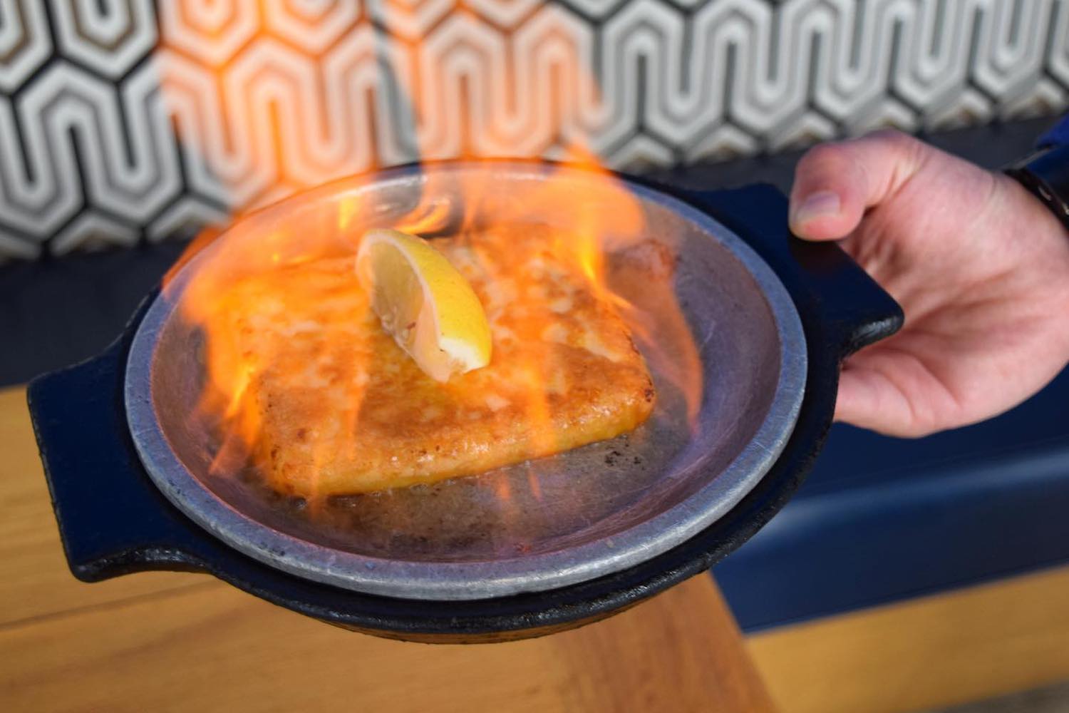a flaming dish of saganaki on a blue plate with a lemon on top