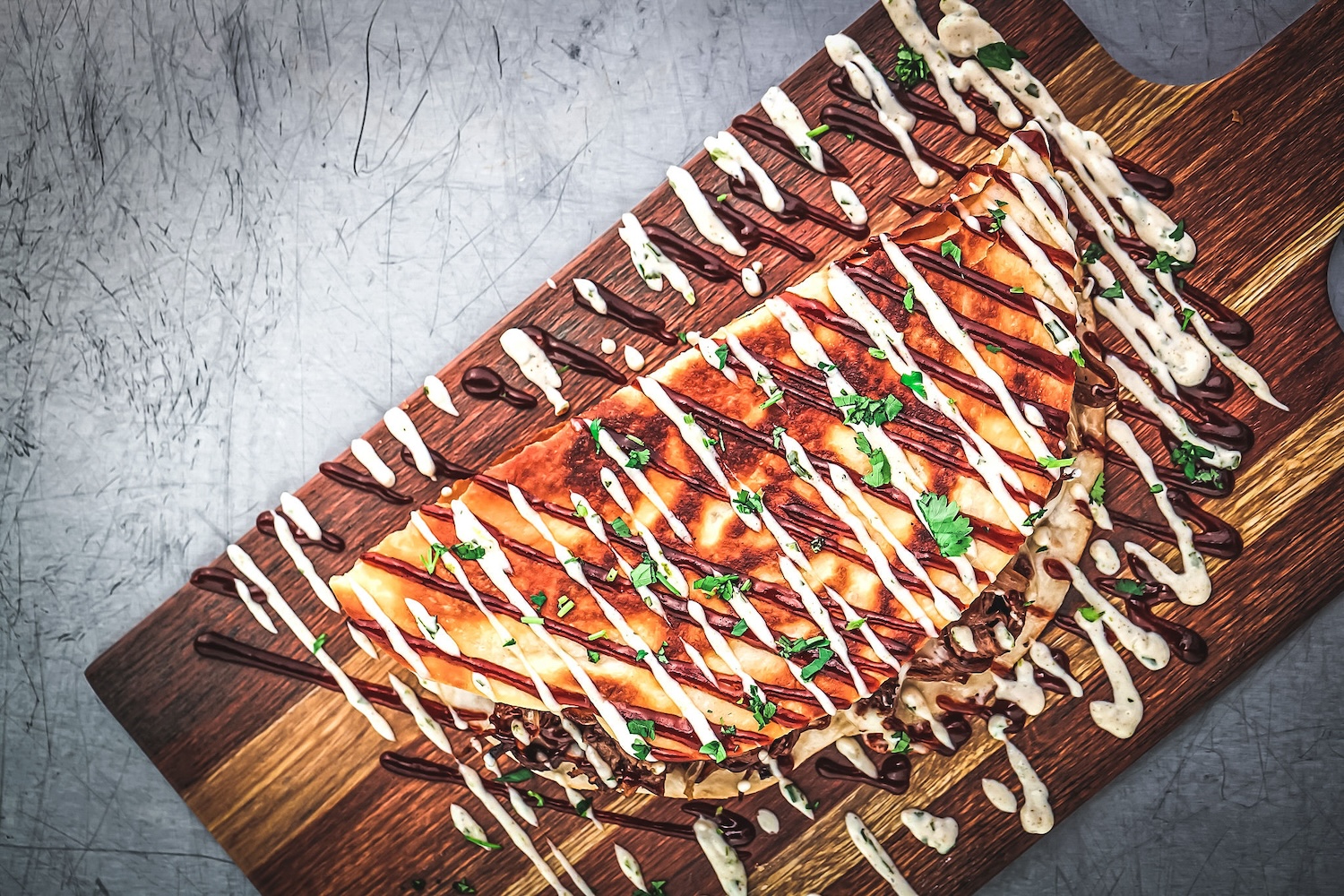 quesadilla with meat inside white sauce drizzled over, green onions, on a wooden board