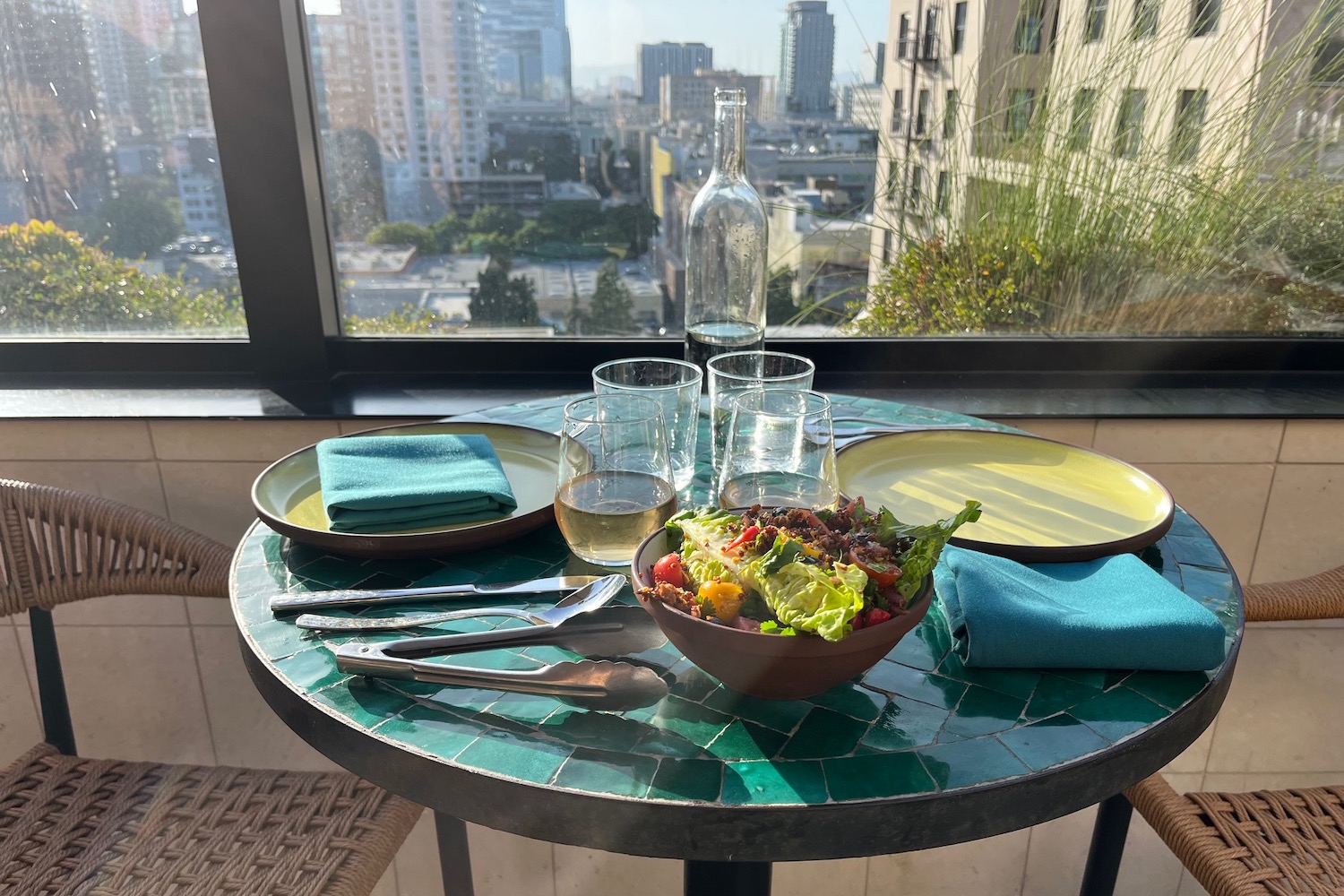 A set table at Cabra, including a garden salad, glasses of white wine, and a stunning view of Downtown Los Angeles.