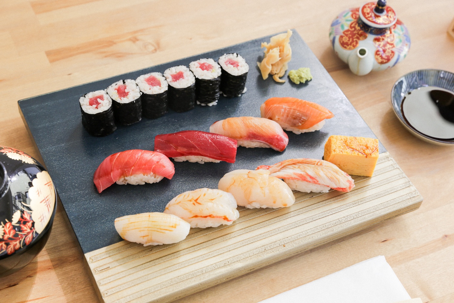 pieces of sashimi on rice and sushi, teapot, soy sauce on sauce plate