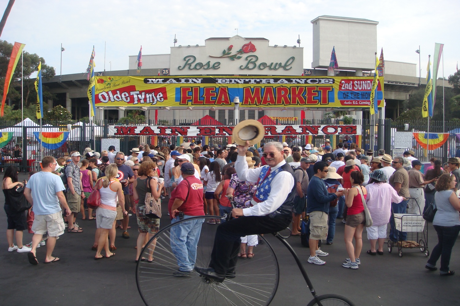 old man on a unicycle holding his hat in front of crowd and sign