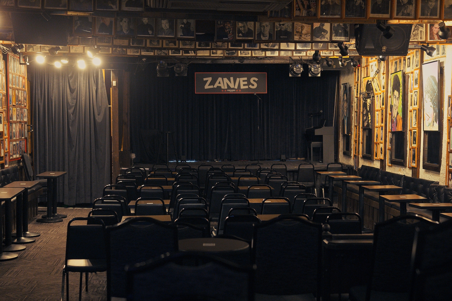 An empty stage with chairs in front of it in a dim room with large posters on the walls.