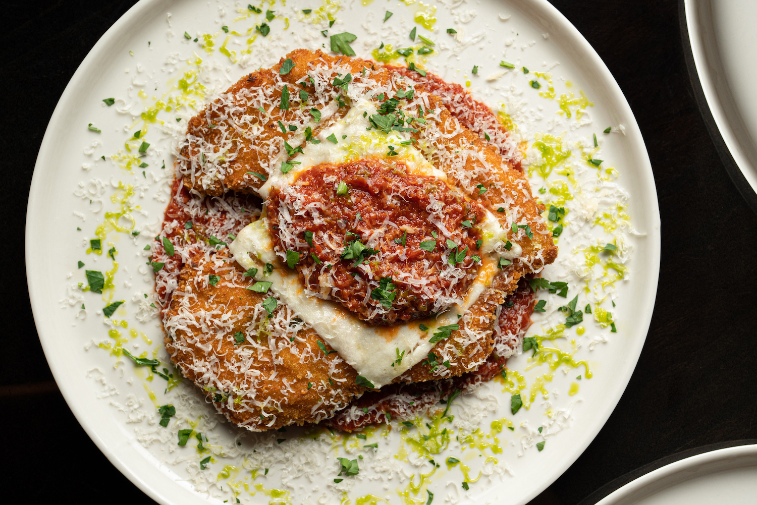 a white plate of chicken parm dusted with cheese, parsley and lemon zest