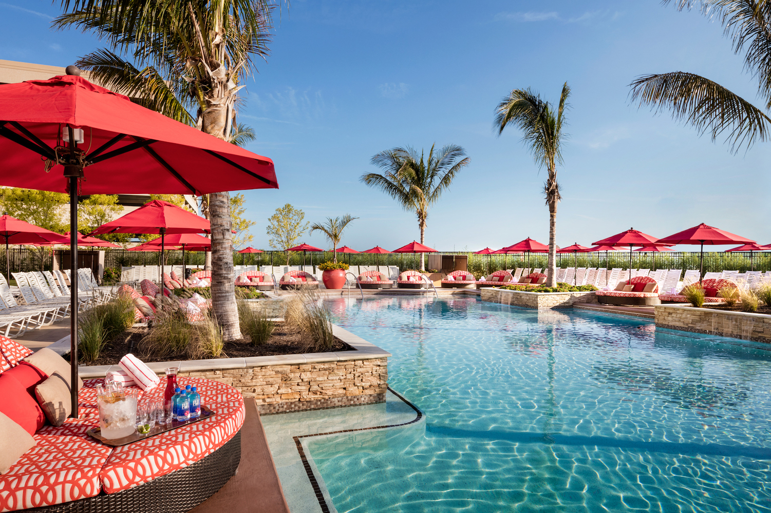 a blue pool surrounded by palm trees and red umbrellas