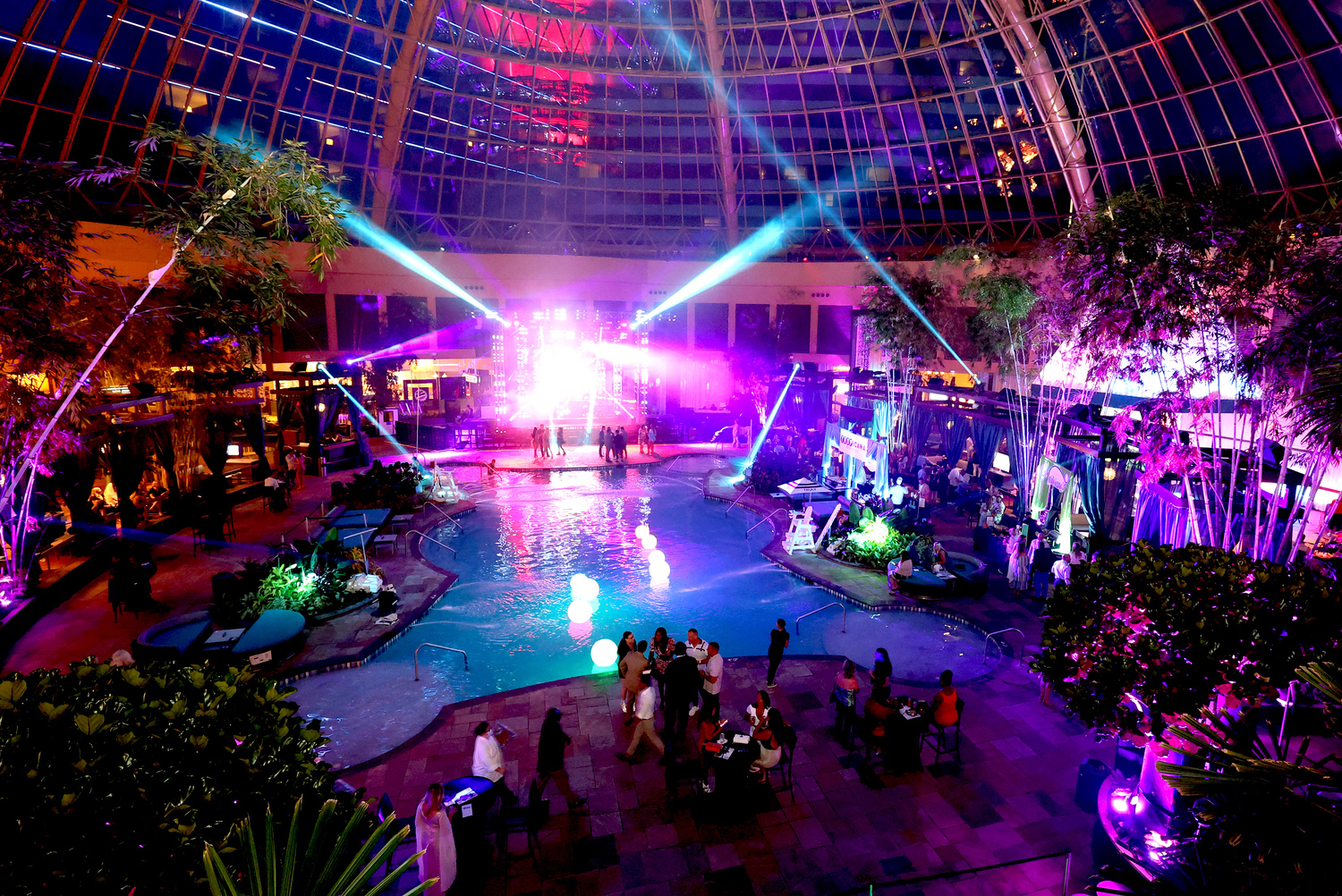 an indoor swimming pool with a domed window ceiling, cabanas and laser lights
