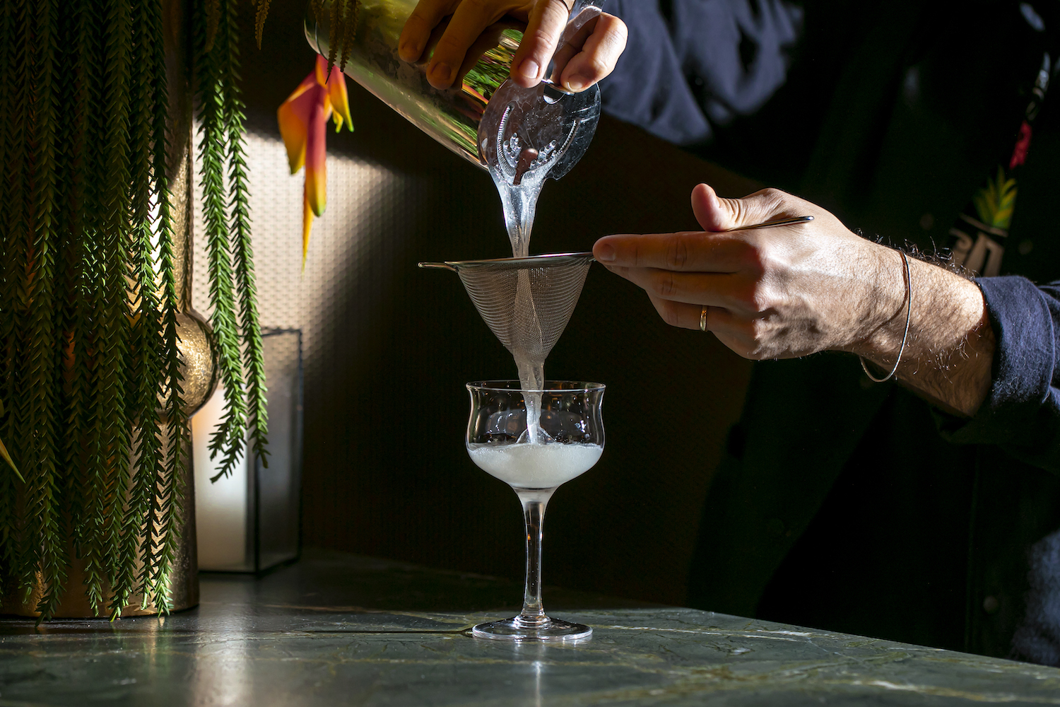 Bartender straining a daiquiri from a cocktail shaker into a coup glass.