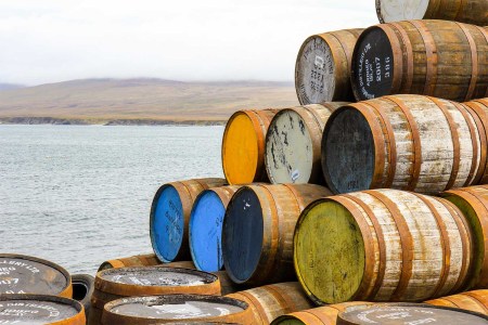 Ardbeg and other scotch whisky barrels stacked at the Bunnahabhain distillery on the isle of Islay, with Jura misty in the background.