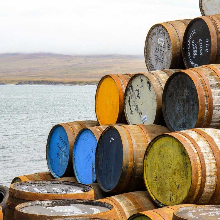 Ardbeg and other scotch whisky barrels stacked at the Bunnahabhain distillery on the isle of Islay, with Jura misty in the background.