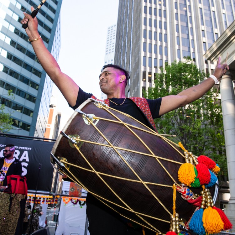 a man playing a giant drum outside with tassels hanging from it