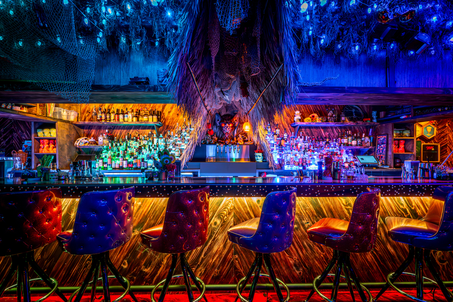 Interior shot of Paradise Lost's bar, with different-colored lights and bar stools decorated in a tiki theme
