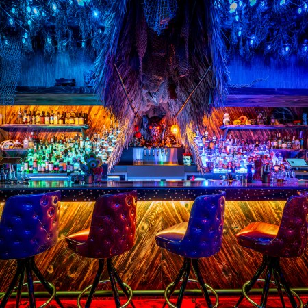Interior shot of Paradise Lost's bar, with different-colored lights and bar stools decorated in a tiki theme
