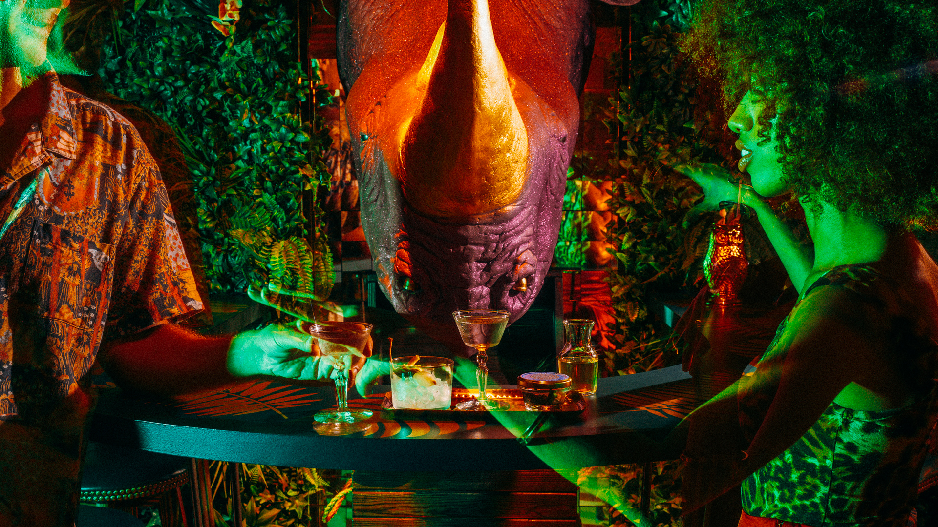 Close-up of a bar with people sitting at it with drinks and there's a 3D purple rhinoceros face behind the bar.