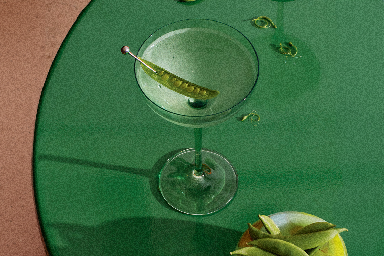 a martini garnished with a snap pea sitting on a green table