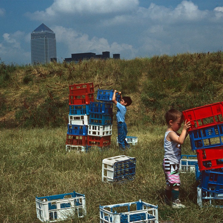 A pair of young boys playing with crates in a field.