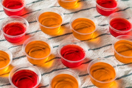 Homemade red and orange jello Shots in Plastic Cups on a striped towel