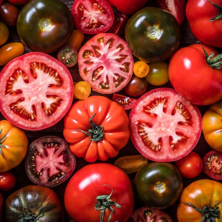 Top view of a background made with various kinds of tomatoes mixed by varieties, sizes and colors. Predominant colors are red, orange and yellow.