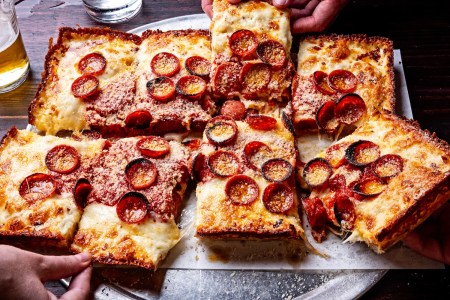 two hands reaching for slices of detroit-style pepperoni pizza