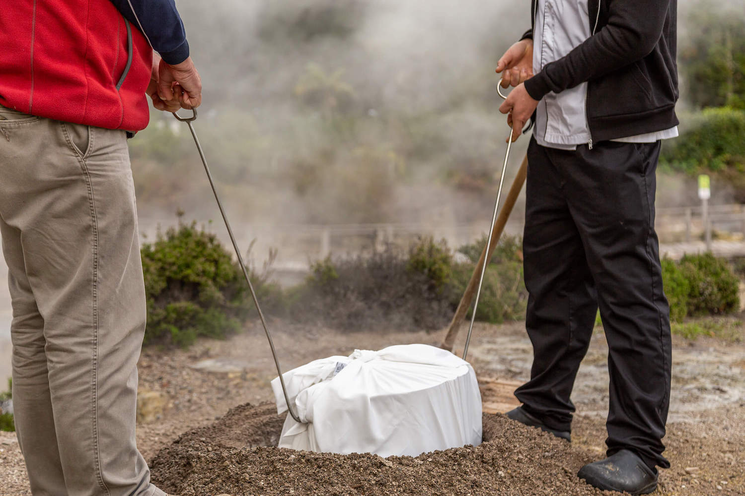 two men lowering a pot wrapped in white cloth into a hole in the ground