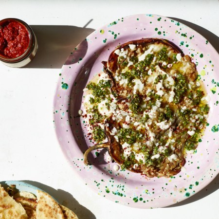 roasted eggplant dip on a speckled pink plate next to a plate of pita and jar of hot sauce