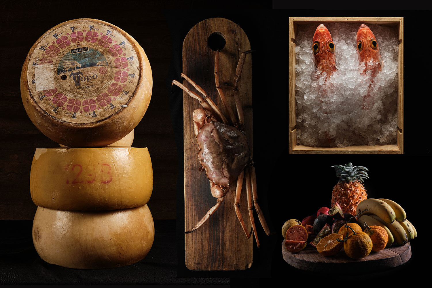 wheels of cheese, a crab, fish in a box of ice and a platter of tropical fruit on a black background