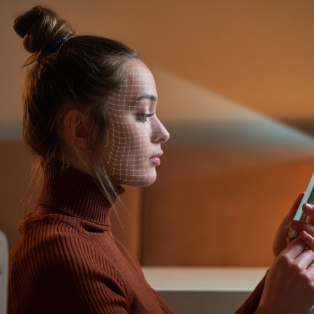 A woman using her selfie camera on her phone to scan her face for facial recognition security measures