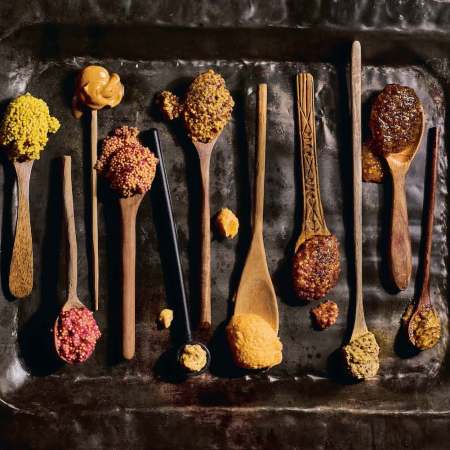 wooden spoons holding different types of mustard on a tin tray