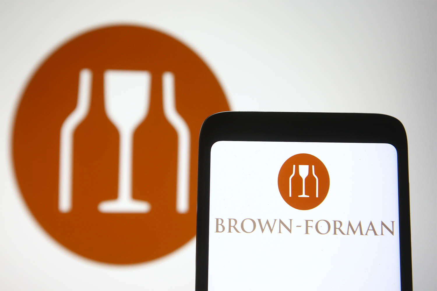 In this photo illustration a BrownForman logo is seen on a smartphone and a pc screen