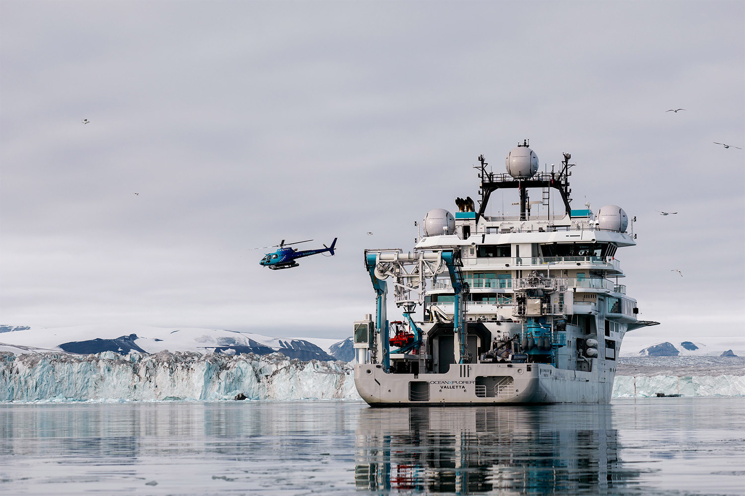 A photo of a helicopter over a ship in the Arctic.