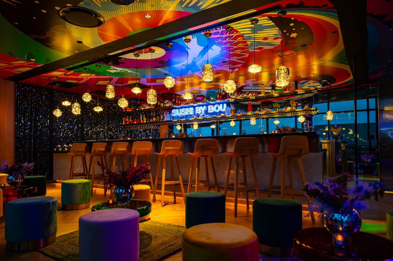 A wide shot of Sushi by Bou's bar area, with colorful sitting stools and shapes projected onto the ceiling