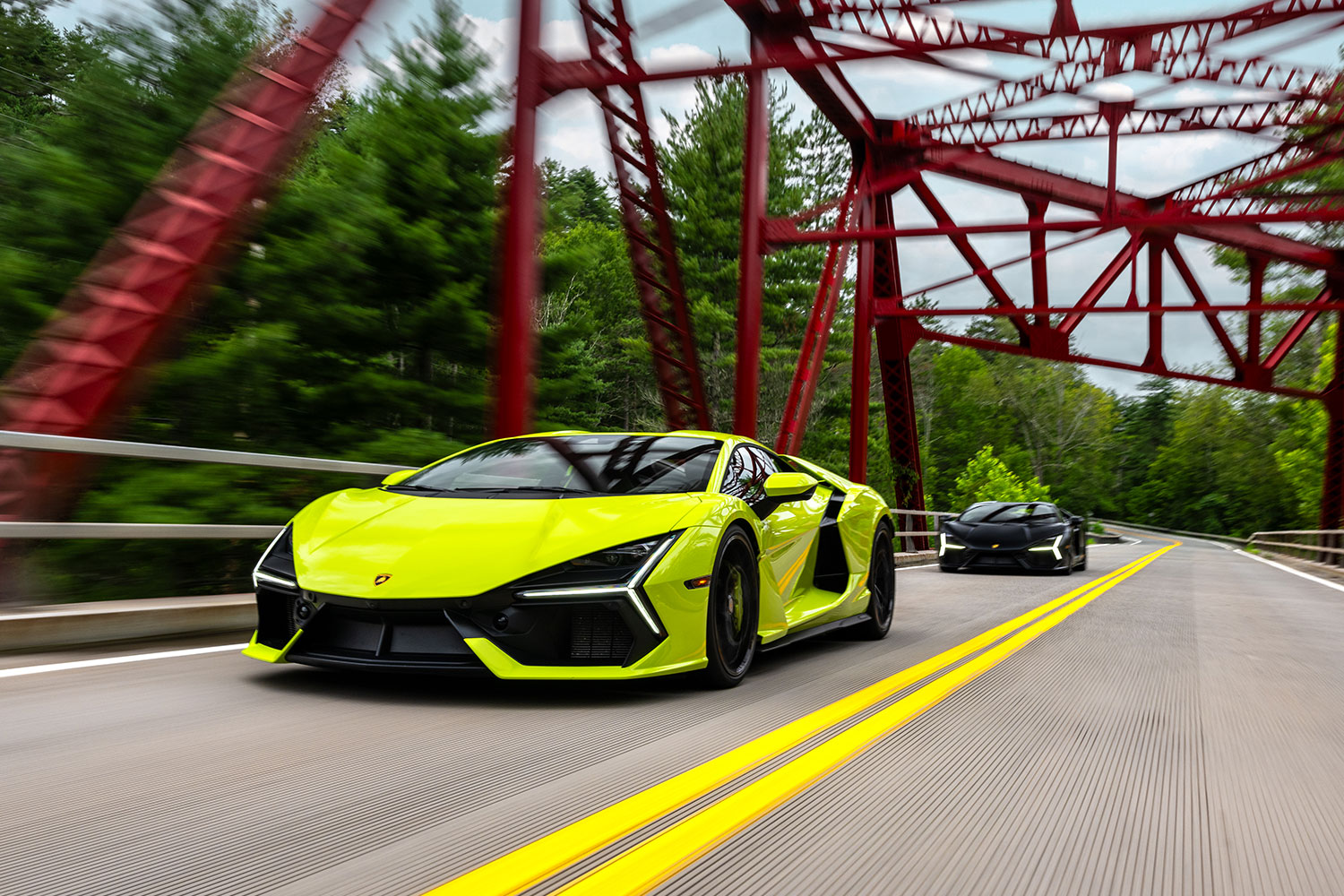 An electric green Lamborghini Revuelto driving across a bridge in front of a black version of the plug-in hybrid supercar