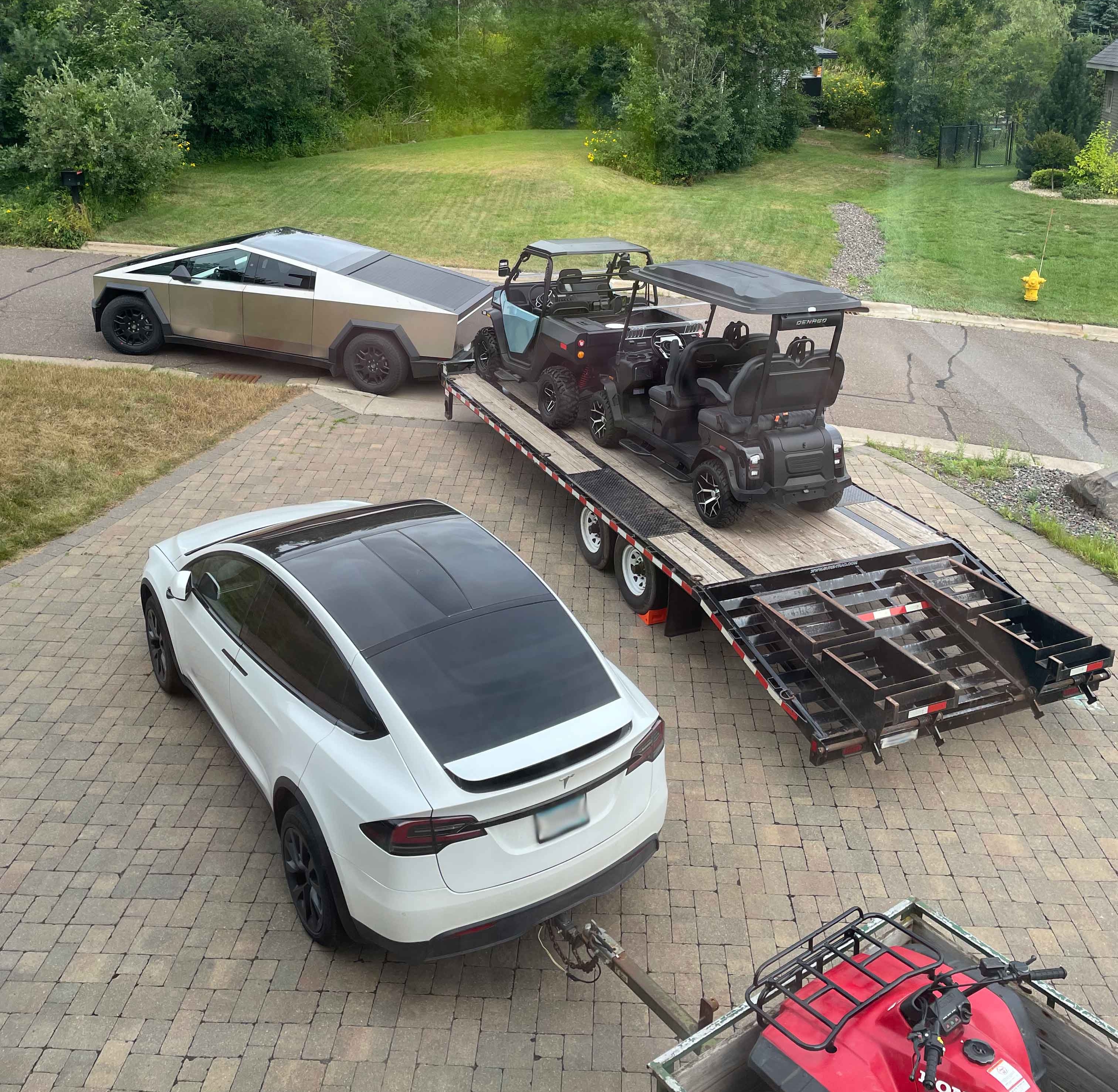 A Tesla Cybertruck towing a trailer loaded with a golf cart and ATV, and a Tesla Model X towing another ATV 