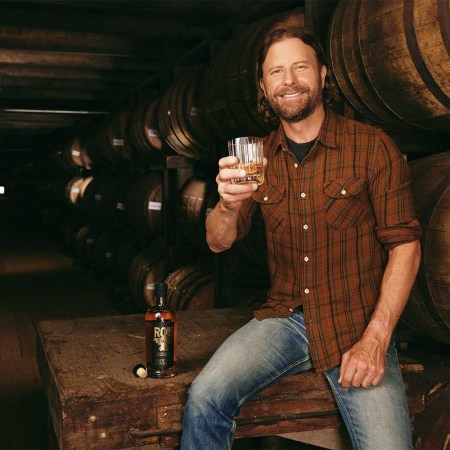 Dierks Bentley holding a glass of whiskey in a rickhouse