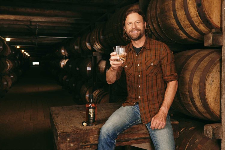 Dierks Bentley holding a glass of whiskey in a rickhouse