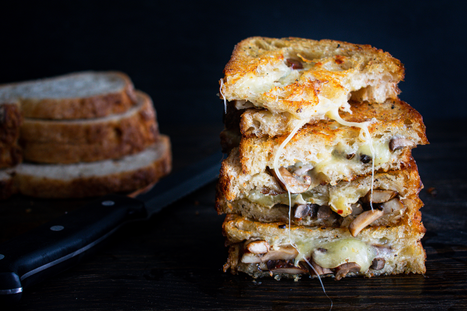 Two sandwiches made with toasted sourdough bread and filled with melted cheese and mushrooms sauteed with garlic