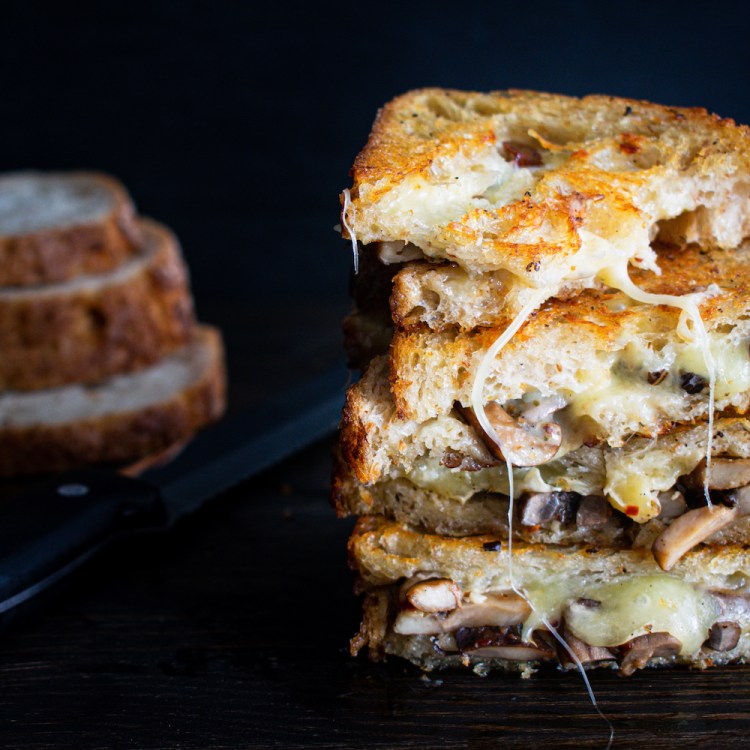 Two sandwiches made with toasted sourdough bread and filled with melted cheese and mushrooms sauteed with garlic