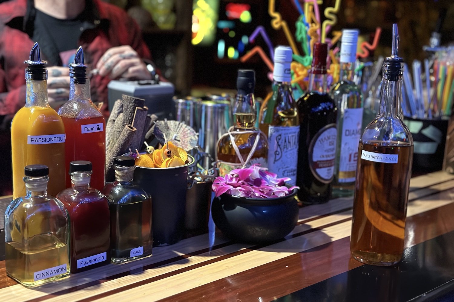 a lineup of rums, tropical garnishes and syrups on a wooden bar top