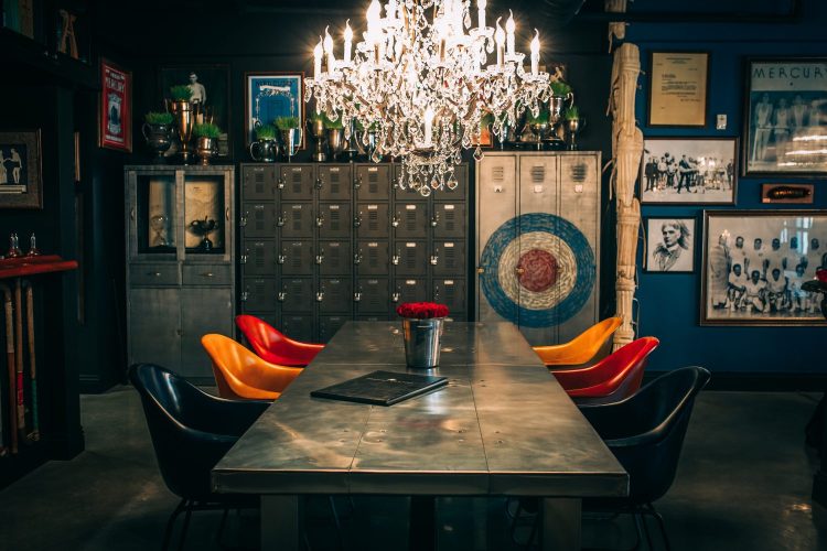 Table with multi-colored seats in front of rustic looking furniture, archery board and a large chandelier