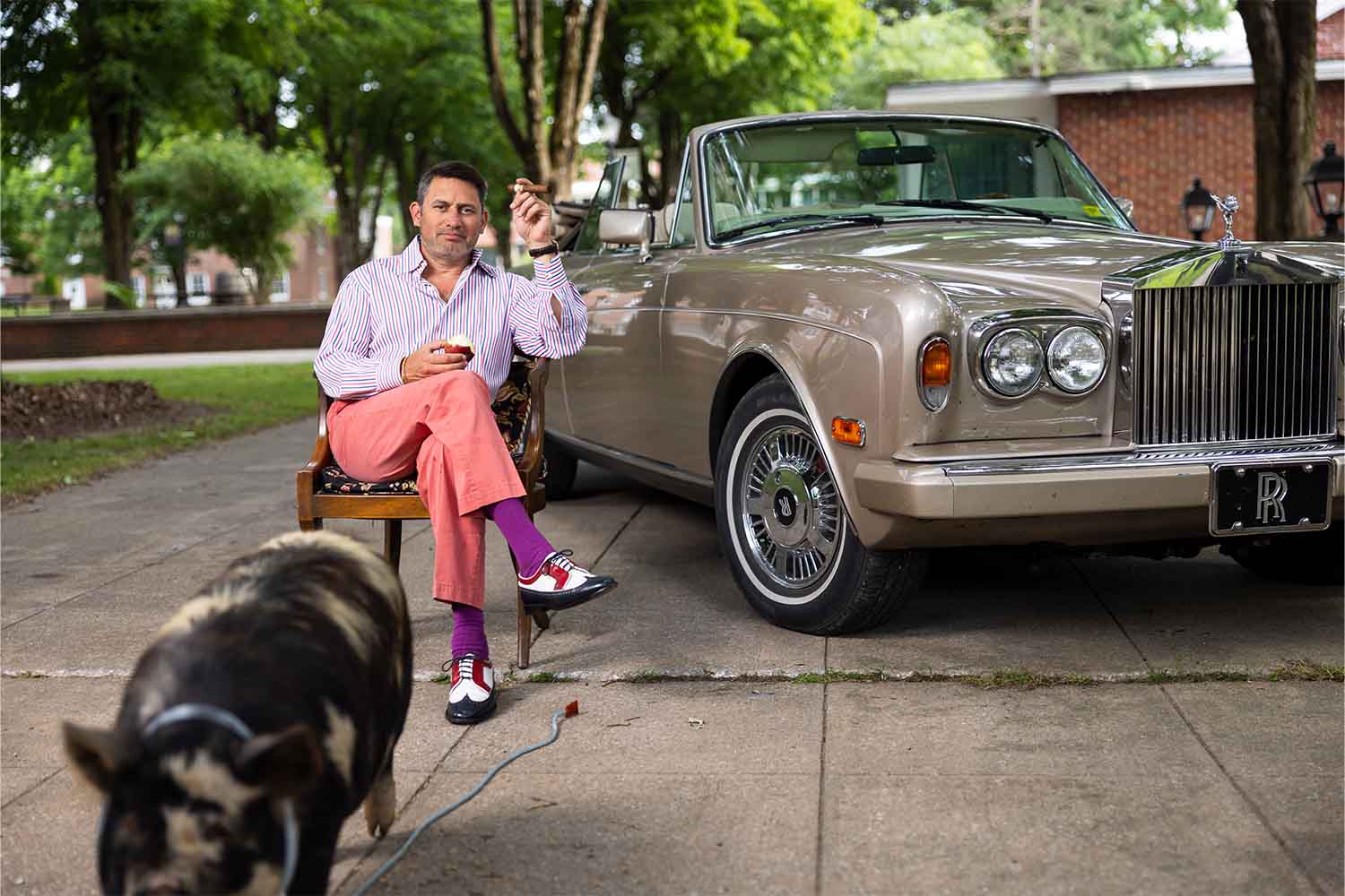 Raj Bhakta and a pig near one of Bhakta's classic cars on the Bhakta campus